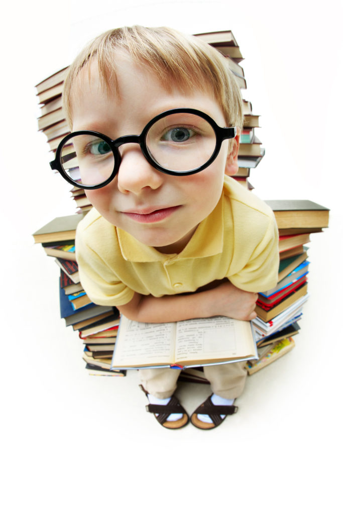 Portrait of diligent pupil sitting on pile of books and looking at camera